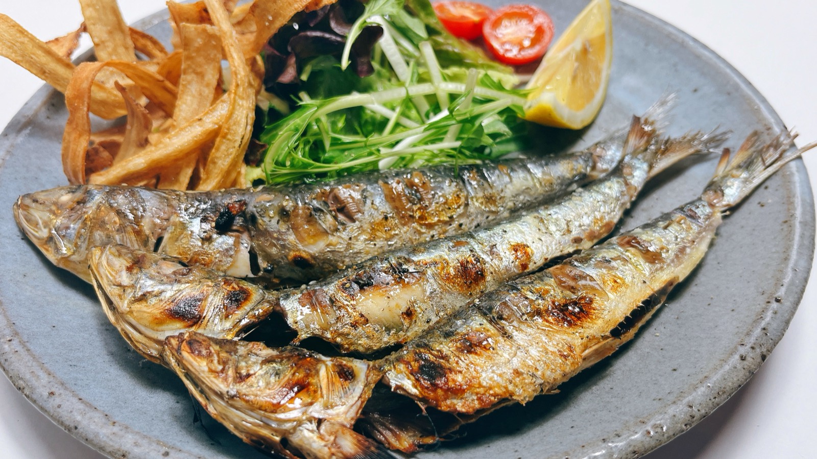 小ぶりの魚を数尾焼き、レモンと薬味を添えた皿