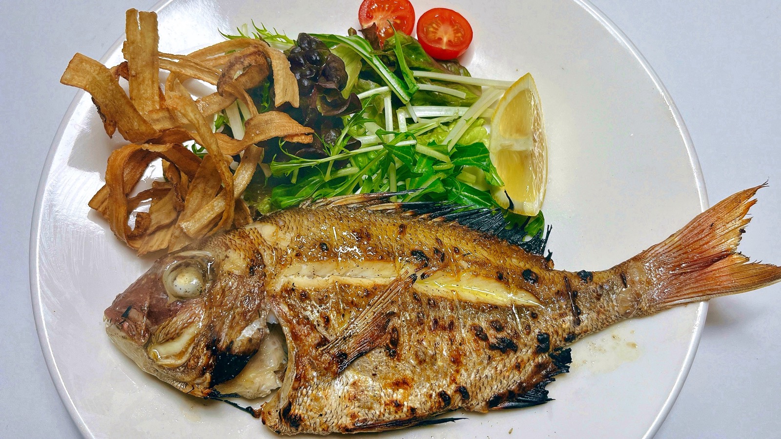 姿のまま焼き上げた魚に、野菜とレモンを添えた一皿